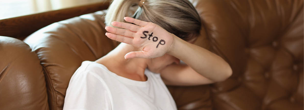 Woman covers her head with hand with word stop while sitting on couch  Concept of domestic violence and discrimination against women 