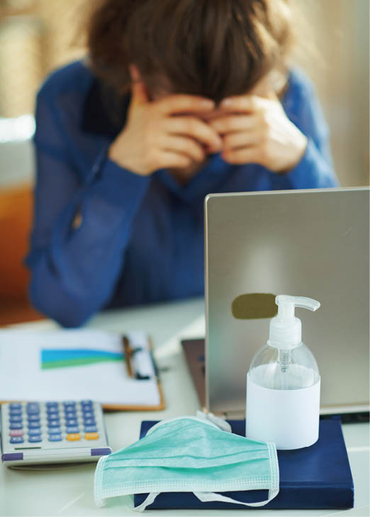 Closeup on medical mask and hand disinfectant and stressed woman in background in temporary home office during the coronavirus epidemic in the house in sunny day 