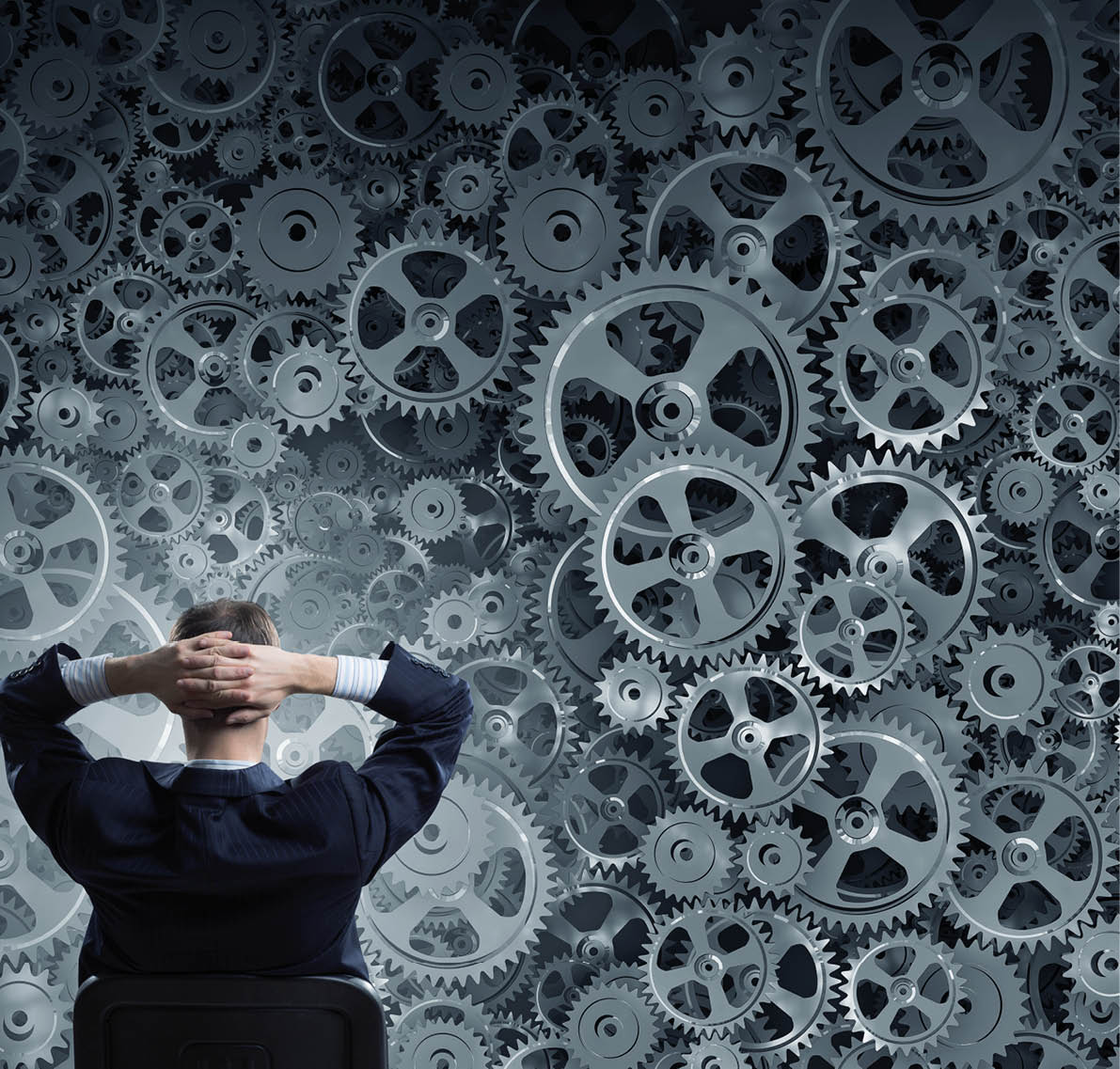Young relaxed businessman sitting in chair and looking at gears mechanism