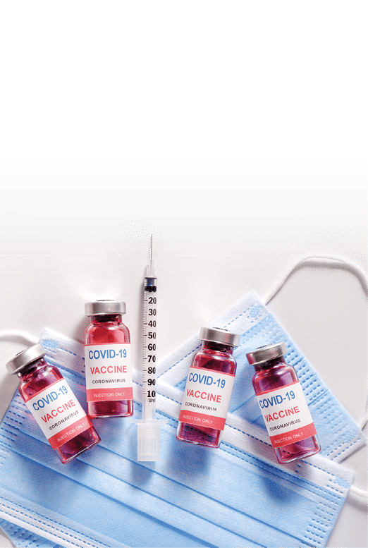 Glass vaccine vials and syringe for vaccination against the COVID-19, SARS-CoV-2 coronavirus pandemic, lying on surgical protective masks, flat lay, copy space, vertical orientation