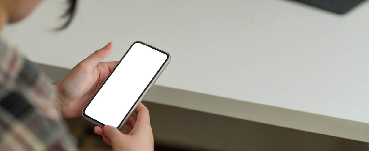 Cropped shot of female holding mock-up smartphone while sitting at minimal workspace