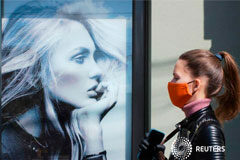 El uso generalizado de mascarillas podría evitar rebrotes de COVID-19 Una mujer con mascarilla camina cerca de un cartel publicitario en Kiev, Ucrania, el 3 de junio de 2020