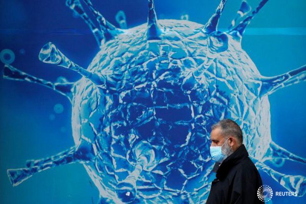 FOTO DE ARCHIVO: Un hombre con una mascarilla camina frente a una ilustración de un virus en el exterior de un centro científico regional en Oldham, Reino Unido, el 3 de agosto de 2020. REUTERS/Phil Noble