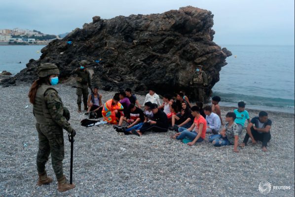 Legionarios españoles se encuentran alrededor de ciudadanos marroquíes, después de que miles de marroquíes nadaron a través de la frontera hispano-marroquí el lunes, en Ceuta, España, el 18 de mayo de 2021. REUTERS/Jon Nazca
