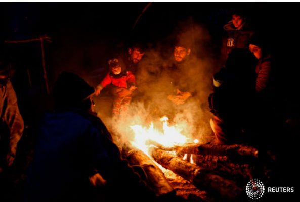 Migrantes se reúnen alrededor de un incendio en un campamento improvisado en la frontera bielorruso-polaca en la región de Grodno, Bielorrusia, el 14 de noviembre de 2021. Fotografía tomada el 14 de noviembre de 2021. Oksana Manchuk/BelTA/Folleto vía REUTERS