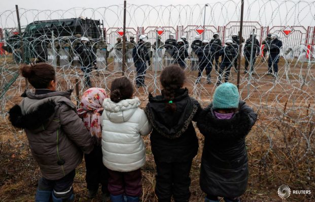 Los niños se paran frente a una valla y se dirigen a los agentes de la ley polacos, que se encuentran al otro lado de la frontera, en la frontera bielorruso-polaca en la región de Grodno, Bielorrusia, el 17 de noviembre de 2021. Maxim Guchek/BelTA/Handout vía REUTERS