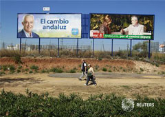 una pareja pasa por delante de dos carteles electorales del presidente de la Junta de Andalucía