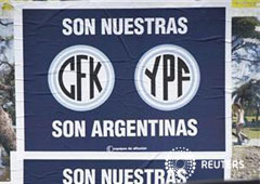 un hombre habla por su móvil dentro de su coche junto a un letrero que reivindica la propiedad argentina de las empresas CFK - YPF, en Buenos Aires