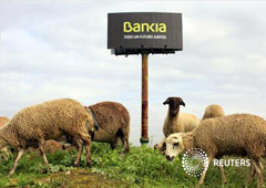 En la imagen de archivo, unas ovejas pastan junto a un cartel de Bnakia a las afueras dee Sevilla, el 4 de diciembre de 2012.