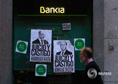 Un hombre pasa junto a una sucursal de Bankia llena de carteles contra el ex consejero delegado de Bankia Rodrigo Rato (I) y Emilio Botín, presidente de Santander, el 8 de junio de 2013 en Madrid