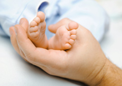 Mano de un padre cogiendo los pies de un bebé