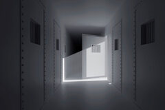 La función preventiva de la prisión permanente revisable Un pasillo de una carcel con las puertas cerradas excepto la de una celda que está abierta y sale luz