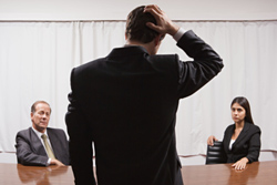 Un ejecutivo rascándose la cabeza mientras escucha a sus jefes en una reunión.