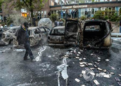 Un transeunte comprueba los daños en una fila de vehículos quemados en el barrio de Rinkeby tras las revueltas de jóvenes en varios suburbios alrededor de Estocolmo, el 23 de mayo de 2013