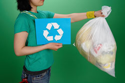 Una mujer con una bolsa de basura en una mano mientras en la otra sostiene el símbolo del reciclaje.