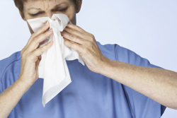 Un hombre estornudando mientras se pone un pañuelo en la nariz.