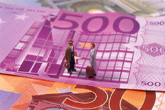 La deducibilidad de los gastos por intereses de demora en el Impuesto sobre Sociedades Figuras de dos hombres sobre billetes de euros