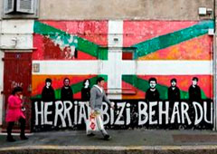 Personas caminando ante un grafiti con una bandera vasca en Bayona, Francia.
