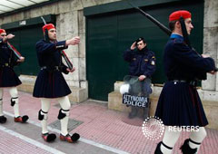 Un policía griego saluda mientras la uardia presidencial marcha en una ceremonia de cambio de guardia en el monumento al soldado desconocido en la plaza Syntagma de Atenas