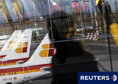 unos aviones de Iberia reflejados en una ventana al pasar una persona durante la huelga de pilotos del 18 de diciembre