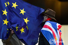 Gana fuerza el plan de un grupo de diputados para impedir un Brexit desordenado Una bandera de la UE junto a dos personas frente al Parlamento Británico, en Londres, el 17 de enero de 2019