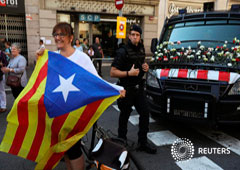 Una mujer con una Estelada (bandera catalana separatista) junto a un coche de los Mossos d'Esquadra lleno de flores tras una manifestación a favor del referéndum del 1 de octubre, en Barcelona, 24 de septiembre de 2017