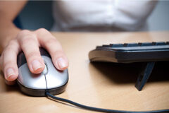 Establecido el régimen de notificaciones de las resoluciones judiciales durante la vigencia del estado de alarma Una persona enfrente del ordenador y con la mano manejando el ratón