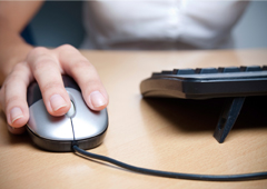 Una persona enfrente del ordenador y con la mano manejando el ratón