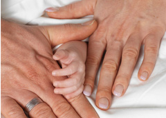 Las manos de dos adultos (hombre, mujer) y en medio la de un bebé