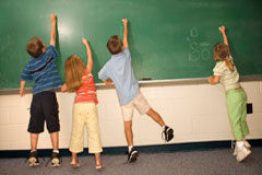 Empieza el curso escolar… ¿Qué tengo que pagar? Cuatro niños de espaldas escribiendo en una pizarra.