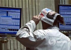 un operador se cubre la cabeza con un diario mientras observa la cotización de la Bolsa de Madrid