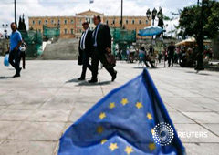 Varias personas pasan jnto a una pequeña bandera de la ÚE en la plaza de la Constitución de Atenas, el 11 de mayo de 2015