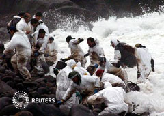 voluntarios limpiando la costa cuando les alcanza una ola en la playa de Cuño, en la provincia de La Coruña, en febrero de 2003
