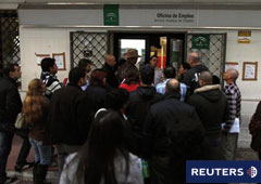 un responsable de seguridad abre la puerta de una oficina de empleo mientras varias personas esperan a entrar en Marbella