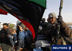 Un combatiente rebelde mira mientras varias personas celebran la retirada de las fuerzas de Gadafi cerca de Ras Lanuf, el 27 de marzo de 2011.