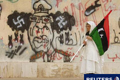 El fiscal CPI vincula a Gadafi con la política de violaciones Una mujer libia con una bandera del reino pasa delante de una caricatura de Muamar Gadafi cerca de la sede de los tribunales en Bengasi, el 8 de junio de 2011.