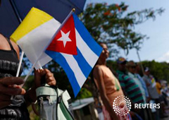 Una mujer sujeta una bandera cubana y una con los colores del Vaticano en una carretera mientras espera al paso del papa Francisco en El Cobre, Cuba, 21 de septiembre de 2015
