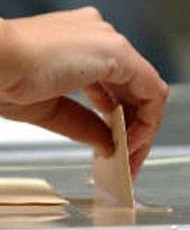 Una persona introduciendo la papeleta en una urna de crista.