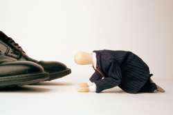 Un muñeco de abogado de rodillas sobre los zapatos de un ejecutivo.