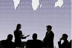 La comunicación del despacho Un grupo hablando entre ellos en una mesa y de fondo una imagen con números binarios y parte del mapa mundi