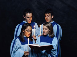Cuatro niños de un coro cantando en la oscuridad con unas velas