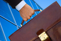 La abogacía itinerante Alguién llevando un maletín marrón y al lado se ve la fachada de un edificio acristalado