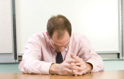 ¿Qué podemos hacer para reducir el impacto negativo que el despido tiene para nuestra organización? Un hombre triste con la cabeza agachada sobre una mesa.