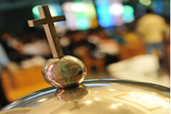 La cancelación del bautismo Una cruz dorada apoyada sobre una pila baustimal y en borroso se ve gente