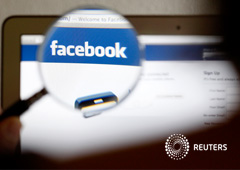 Un hombre enfocando con una lupa en un ordenador la palabra de facebook