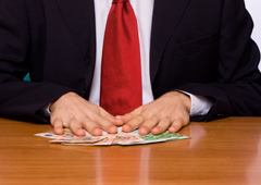 Un hombre sentado y sus manos apoyadas en unos billetes de euros que hay sobre la mesa