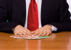 Un hombre sentado y sus manos apoyadas en unos billetes de euros que hay sobre la mesa Un hombre sentado y sus manos apoyadas en unos billetes de euros que hay sobre la mesa