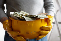 Retribuciones de las vacaciones Persona sujetando un casco de obra con billetes dentro