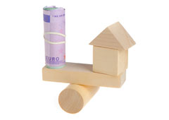 Balanza de madera con una casita y un rollo de billetes de euro