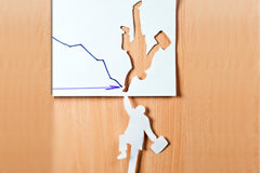 El concurso necesario frente al proceso monitorio en tiempos de crisis En un papel dibujado una flecha hacía abajo y recortado una silueta de un hombre, y esa silueta recortada cuelga hacía abajo